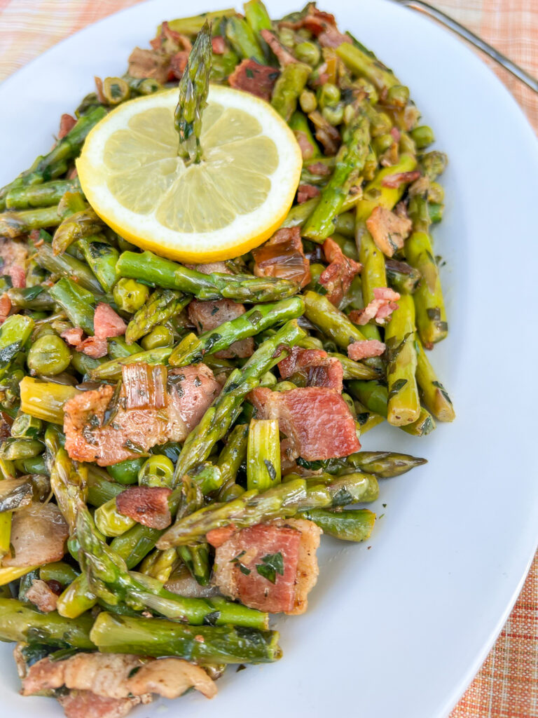 Plated Asparagus and Peas garnished with a slice of lemon on a white plate.