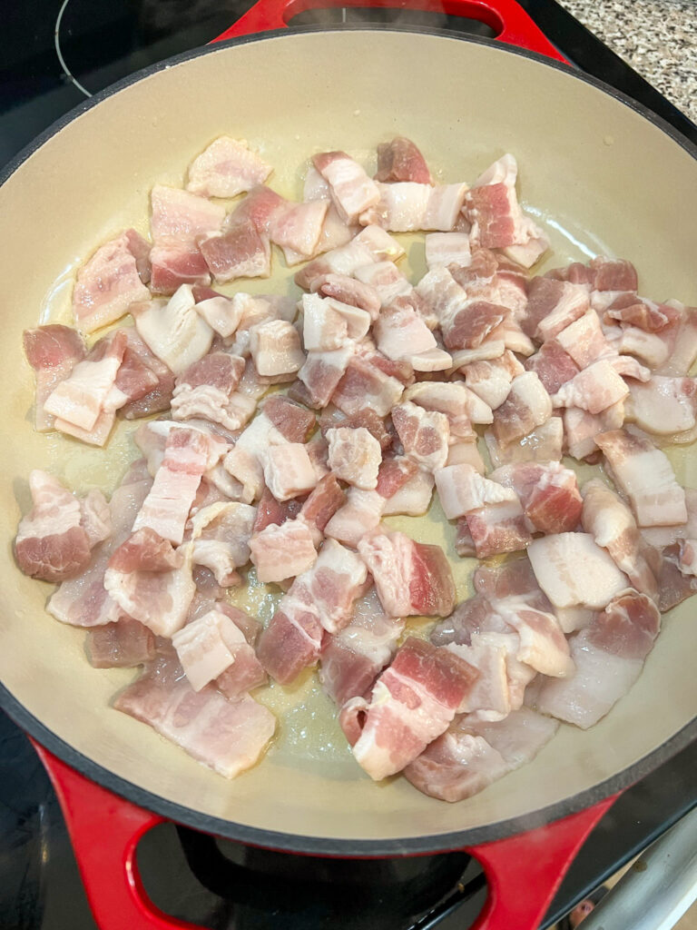 Bacon pieces cooking in an enameled Dutch oven.
