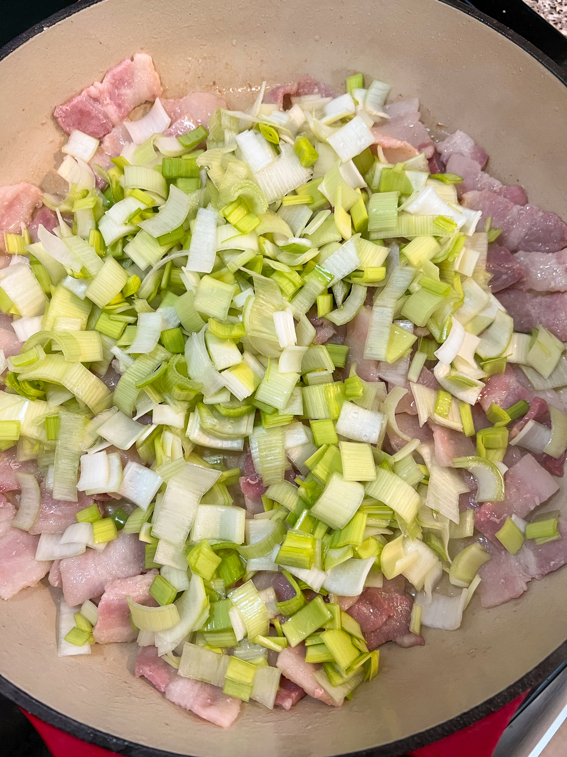 Chopped bacon and leeks cooking together in a Dutch oven.