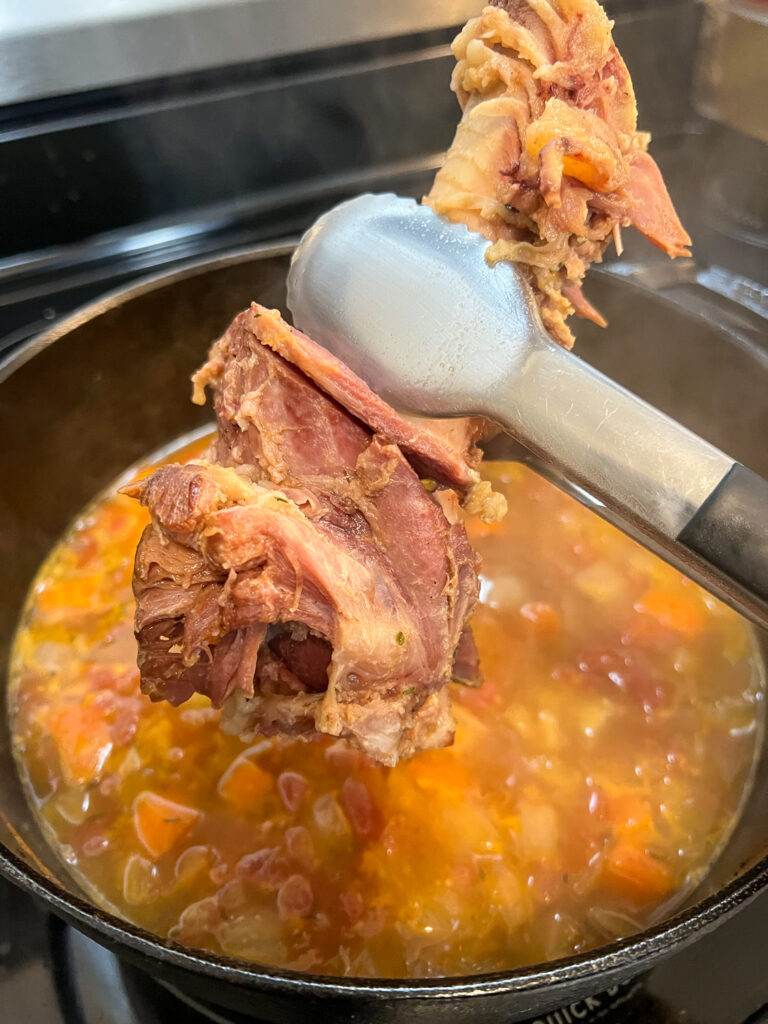 The ham bone is being removed from the boiling soup.