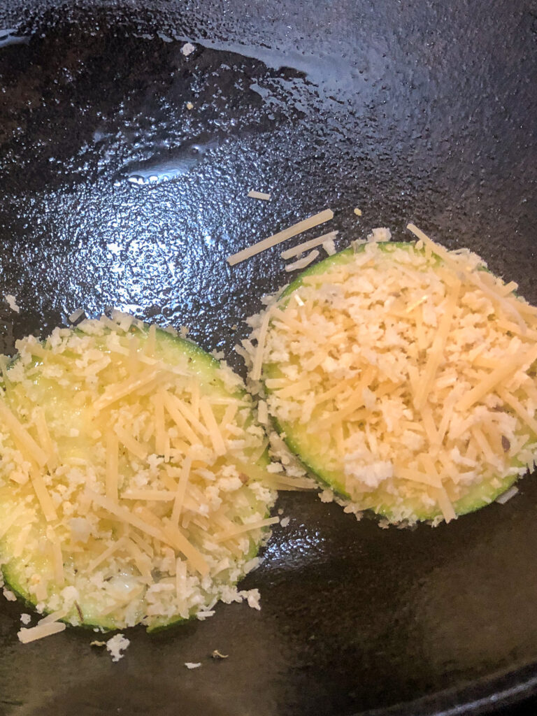 Two Parmesan zucchini chips being placed in a skillet.