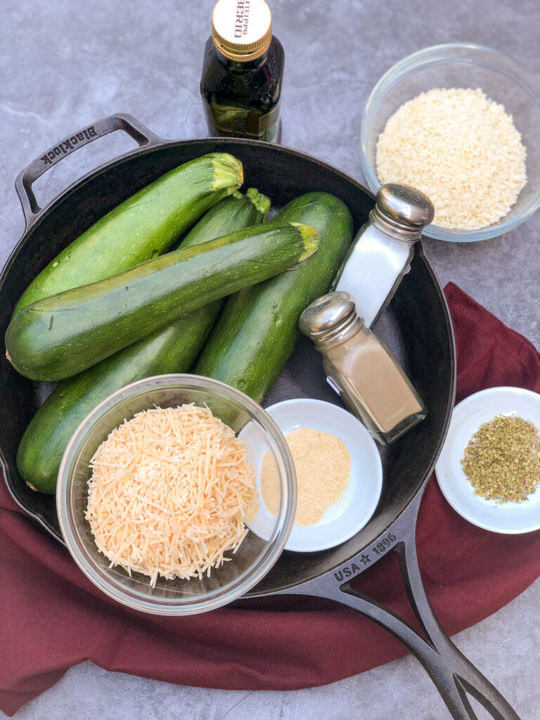 Ingredients to make Parmesan Zucchini Chips: olive oil, panko, zucchini, salt, pepper, Parmesan cheese, granulated garlic, and oregano with the cast iron skillet.