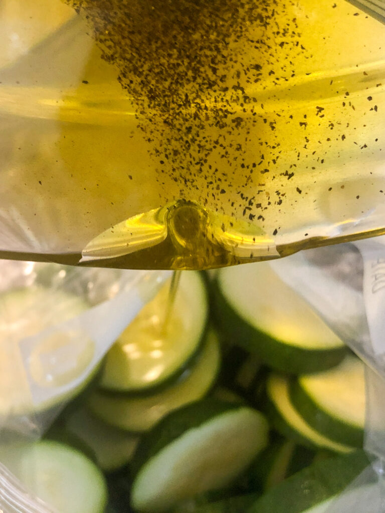 Seasoned olive oil being poured into a bag with the sliced zucchini.