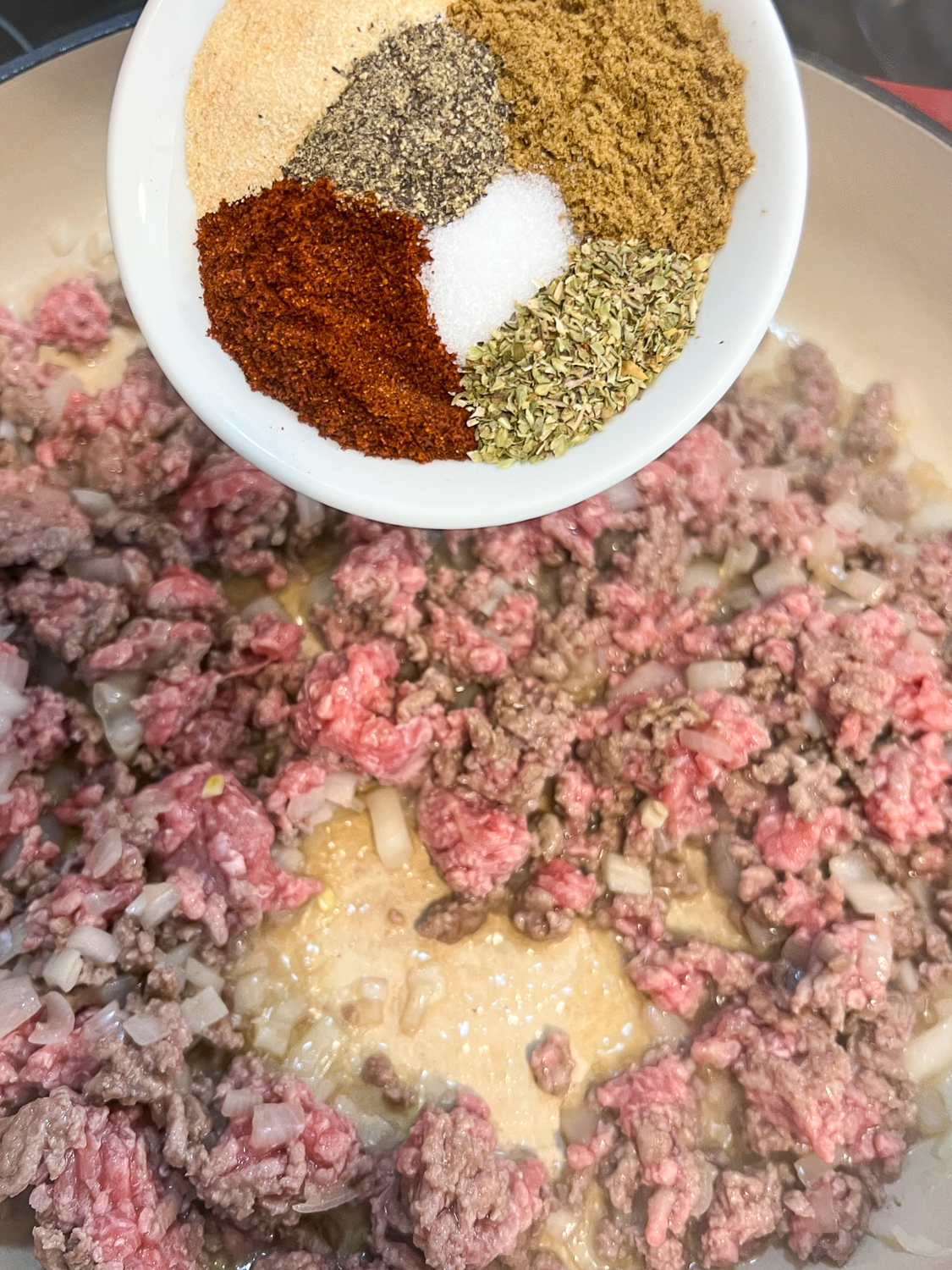 The spices being added to the partially cooked ground beef and onions.