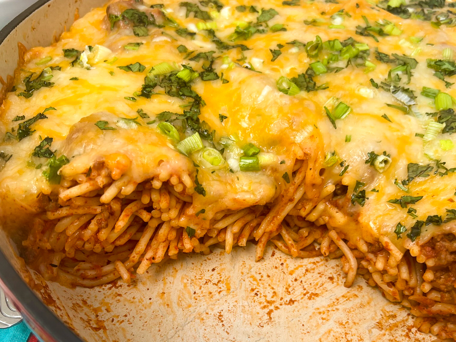 Close up image of Baked Mexican Spaghetti in the skillet with a quarter of it missing to show texture and inside.