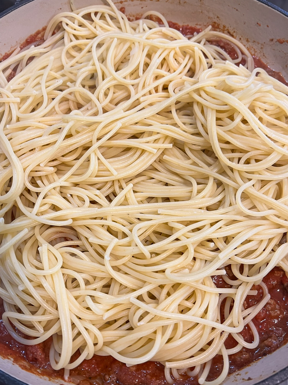 Cooked spaghetti added to the saucy meat mixture.