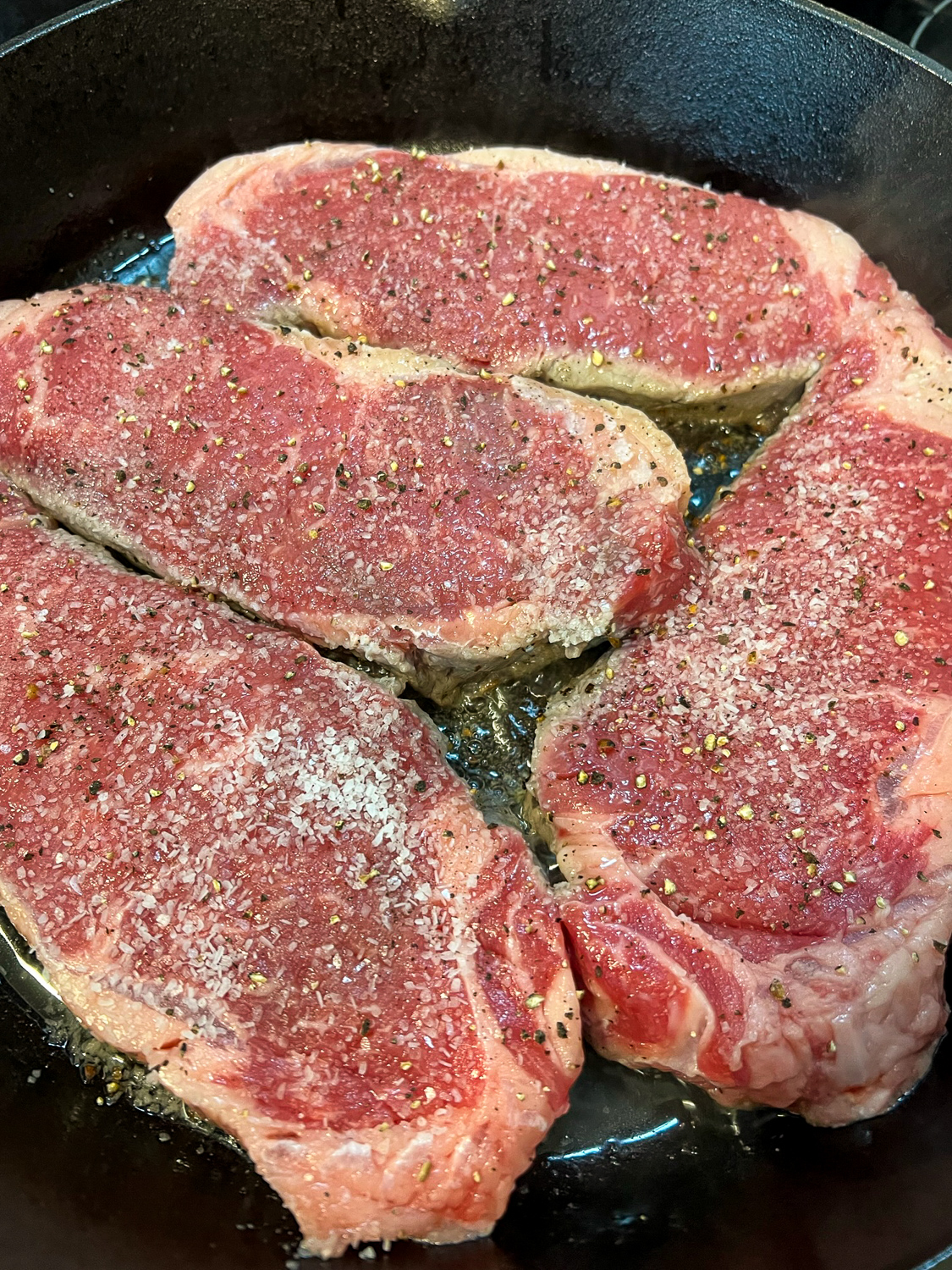 4 steaks in the cast iron skillet cooking on the first side. 