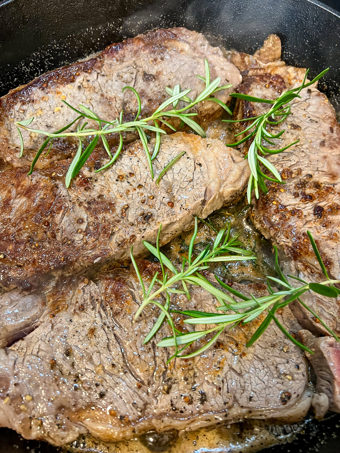 Perfectly seared and cooked steak garnished with fresh rosemary in a skillet.