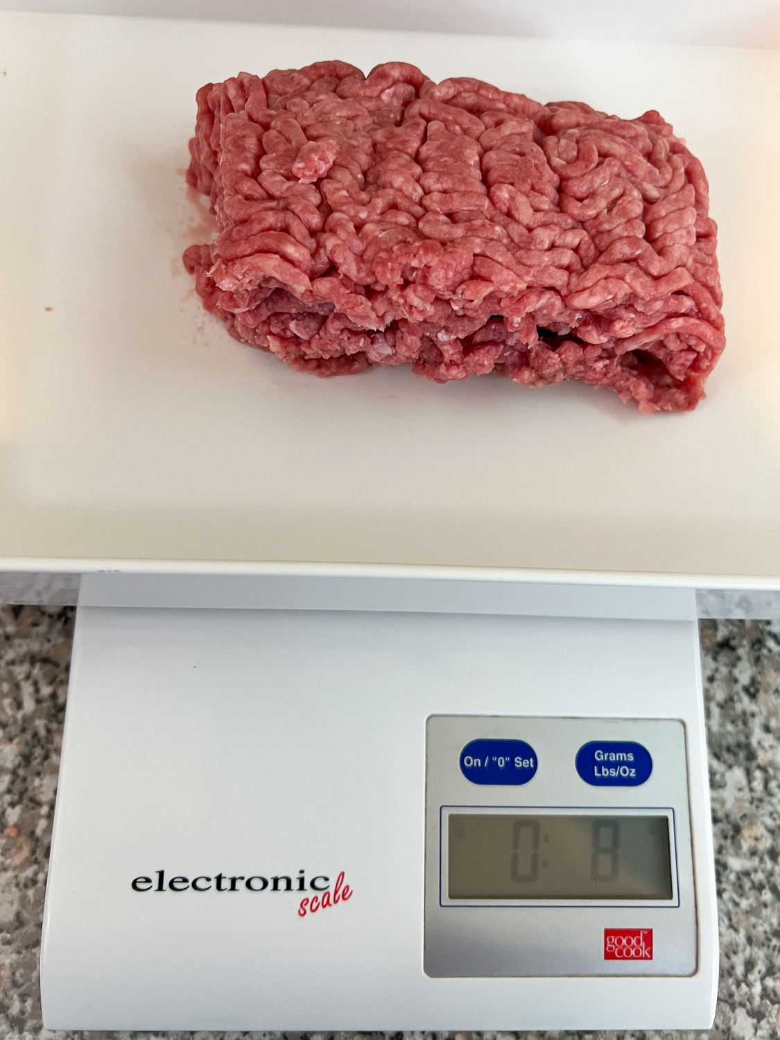 Ground beef on a kitchen scale registering 8 oz or a half pound.