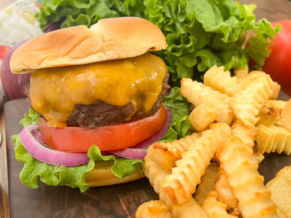 Cheeseburger in a bun with lettuce, tomato, and red onion sitting next to french fries.