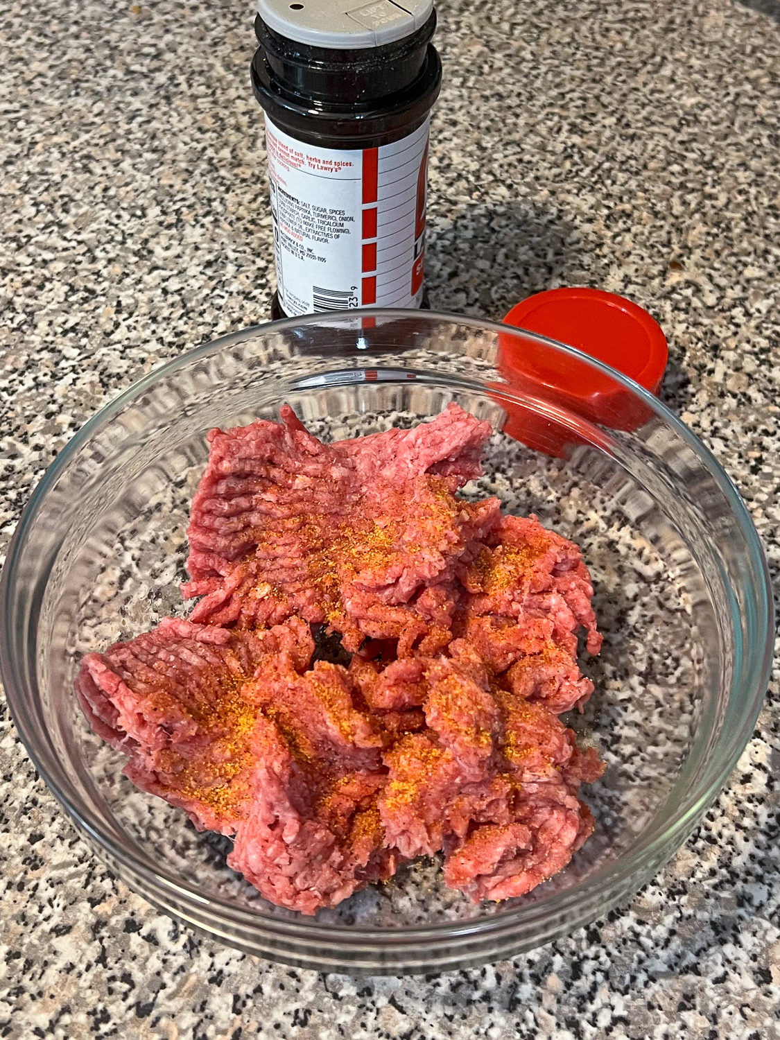 Ground beef in a glass bowl with season salt sprinkled over it.