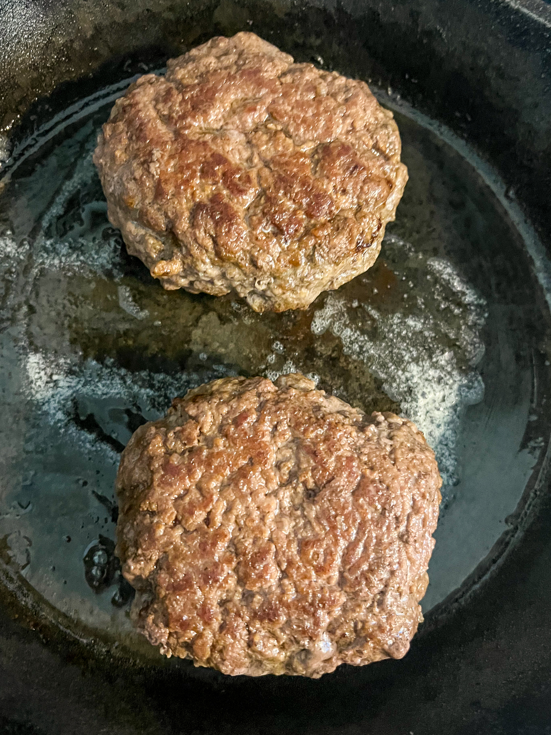Two half pound burgers cooking in a cast iron skillet.