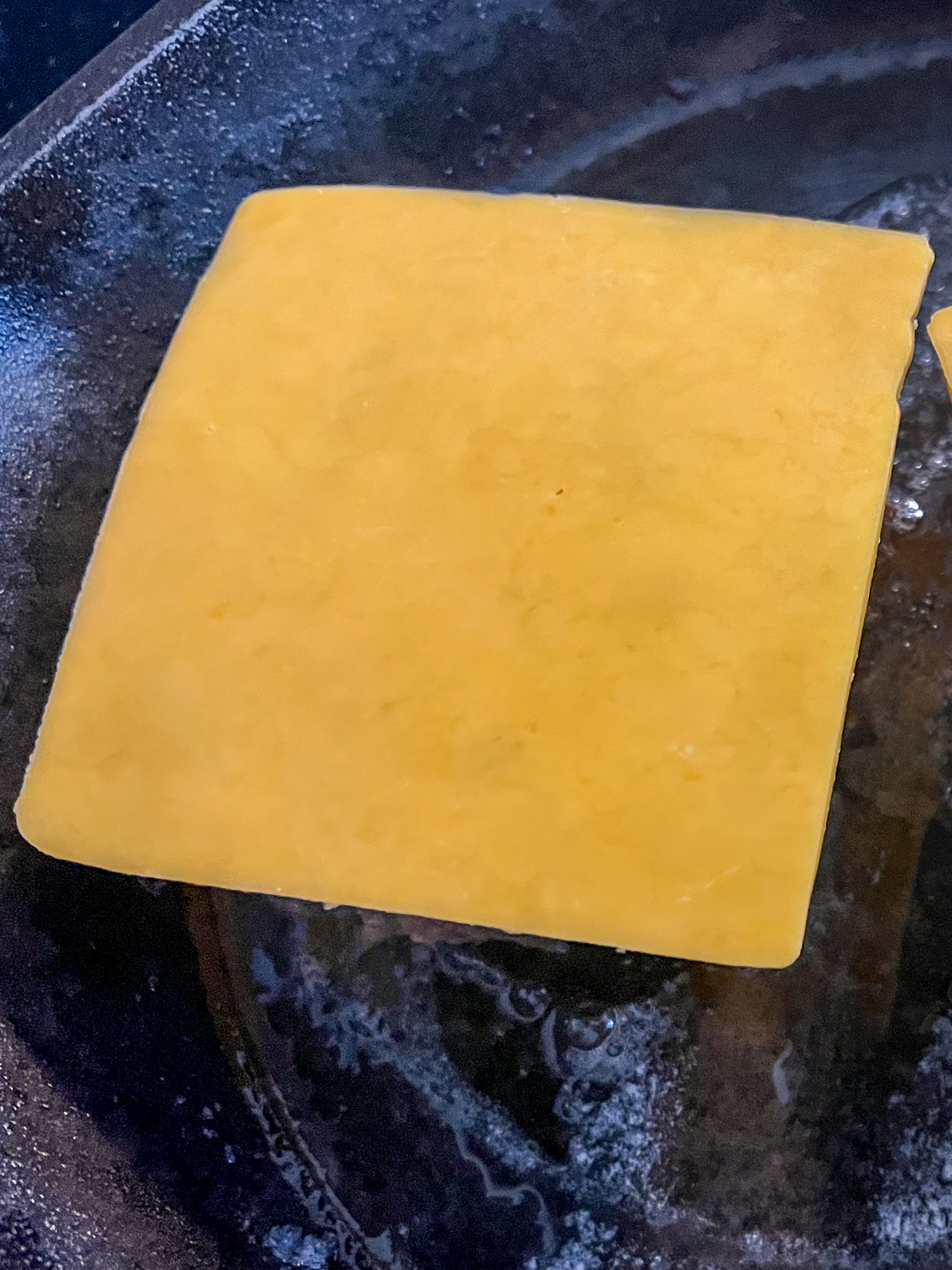 A slice of cheddar cheese placed atop a burger in a cast iron skillet.
