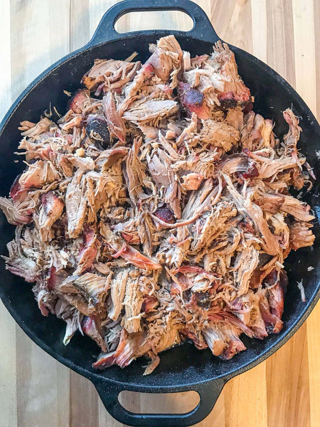 The smoked meat has been shredded for pulled pork inside a cast iron skillet. 