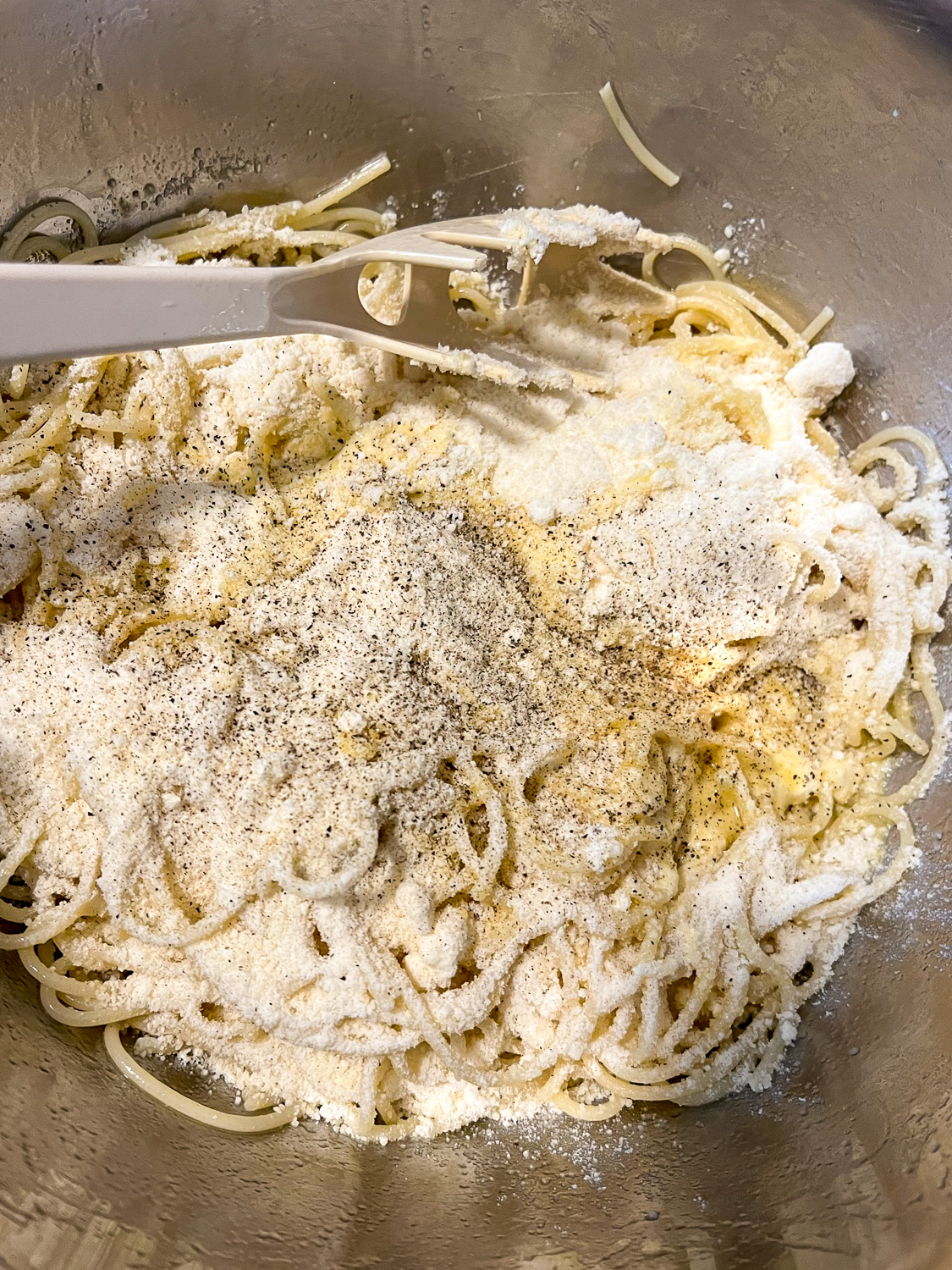 Olive oil, eggs, black pepper, and parmesan cheese being mixed into the spaghetti.
