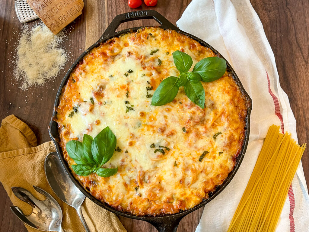 Baked Spaghetti Casserole in a cast iron skillet garnished with fresh basil.
