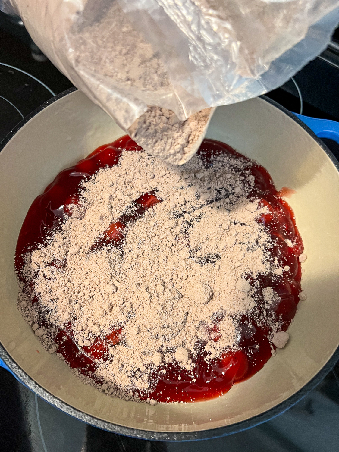 Devil's Food cake mix being sprinkled over the cherry pie filling in the dutch oven.