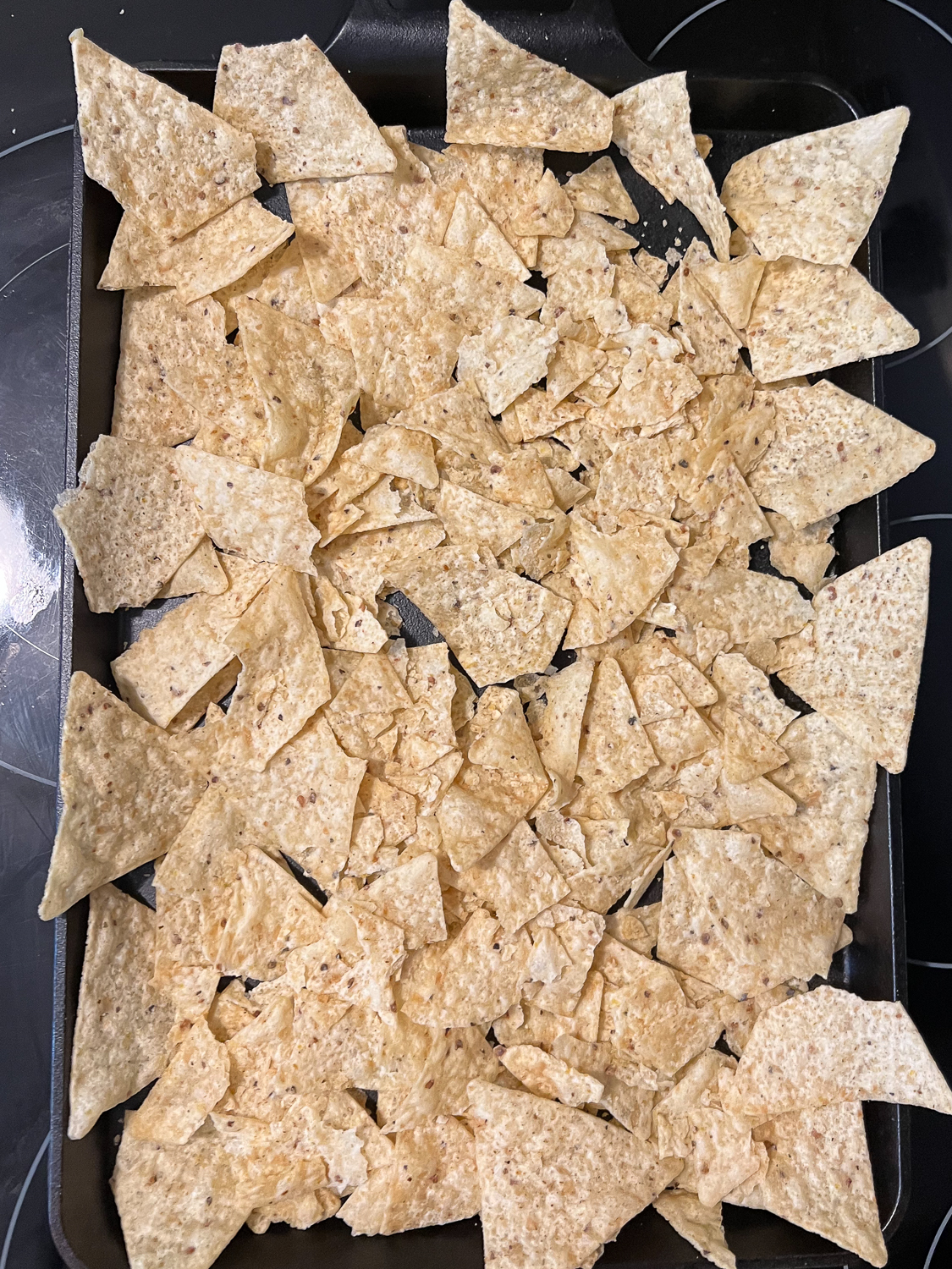 A thin layer of tortilla chips arranged on a cast iron baking tray.