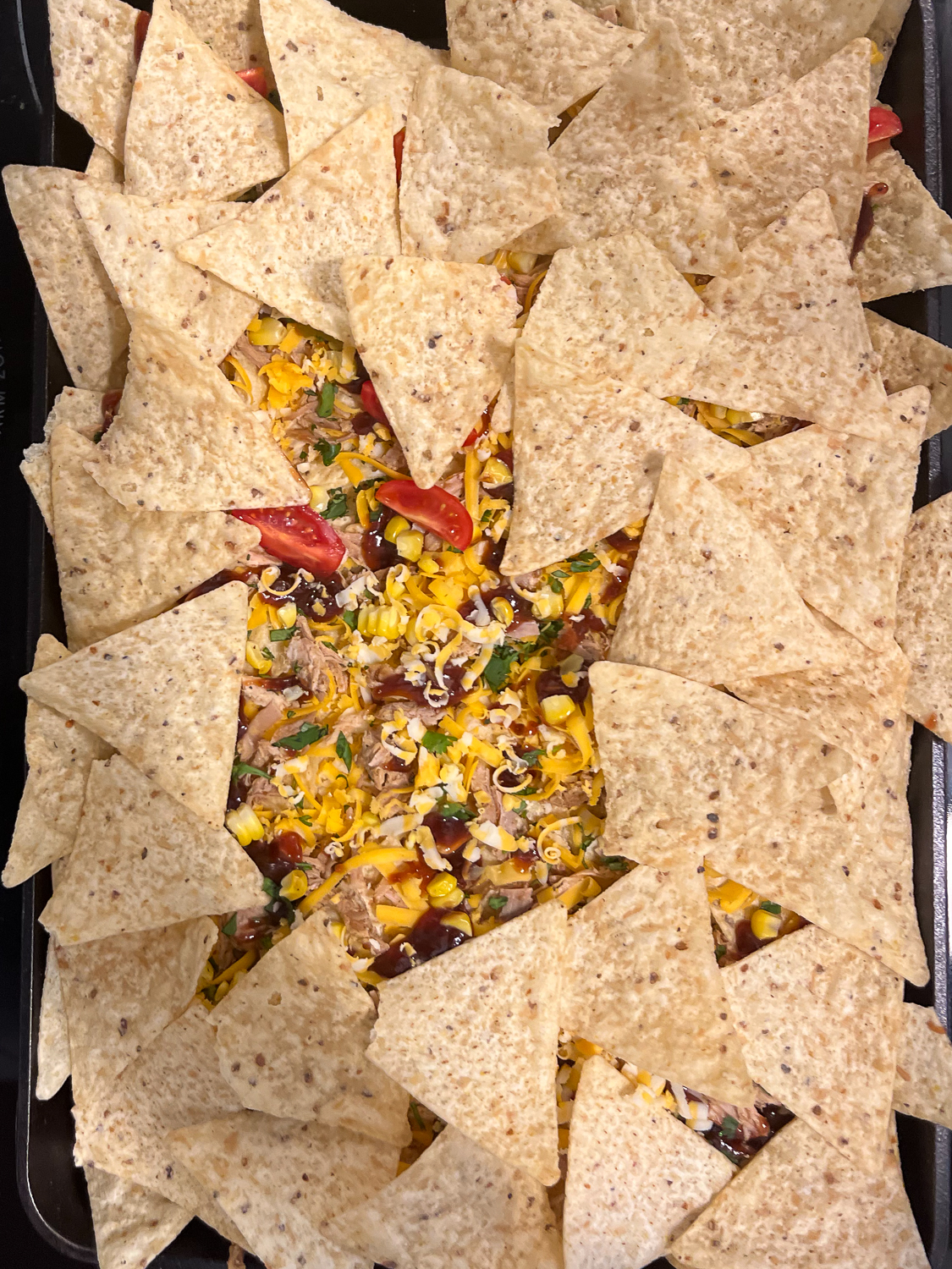 A second layer of chips is added atop the first completed layer of nachos.