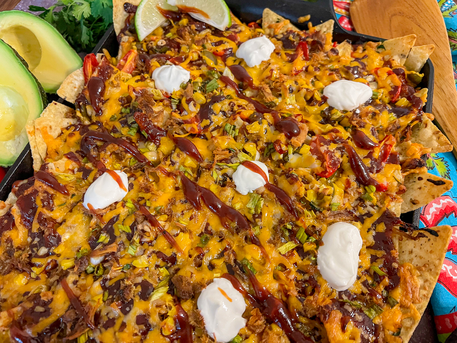 A close up view of pulled pork nachos with dollops of sour cream and drizzle of barbecue sauce.
