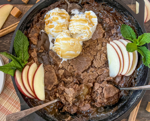 Baked caramel apple cake garnished with scoops of vanilla ice cream and caramel sauce, fresh apple slices and mint along the sides.