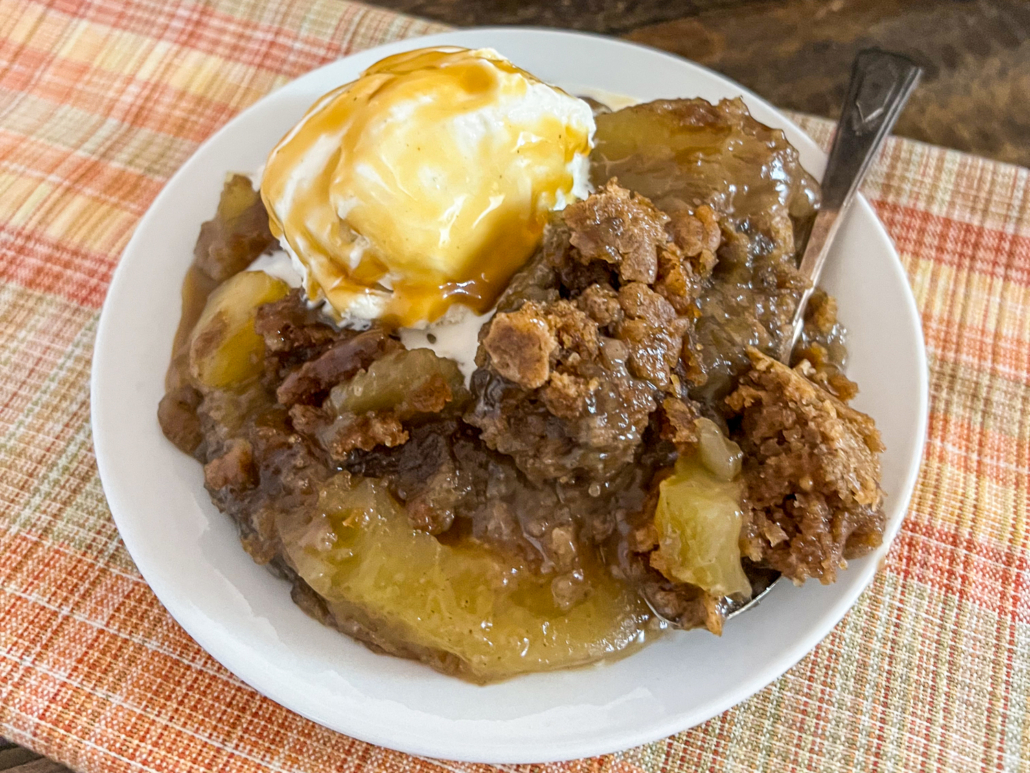 A hearty serving of caramel apple cake with a scoop of vanilla ice cream and caramel sauce.