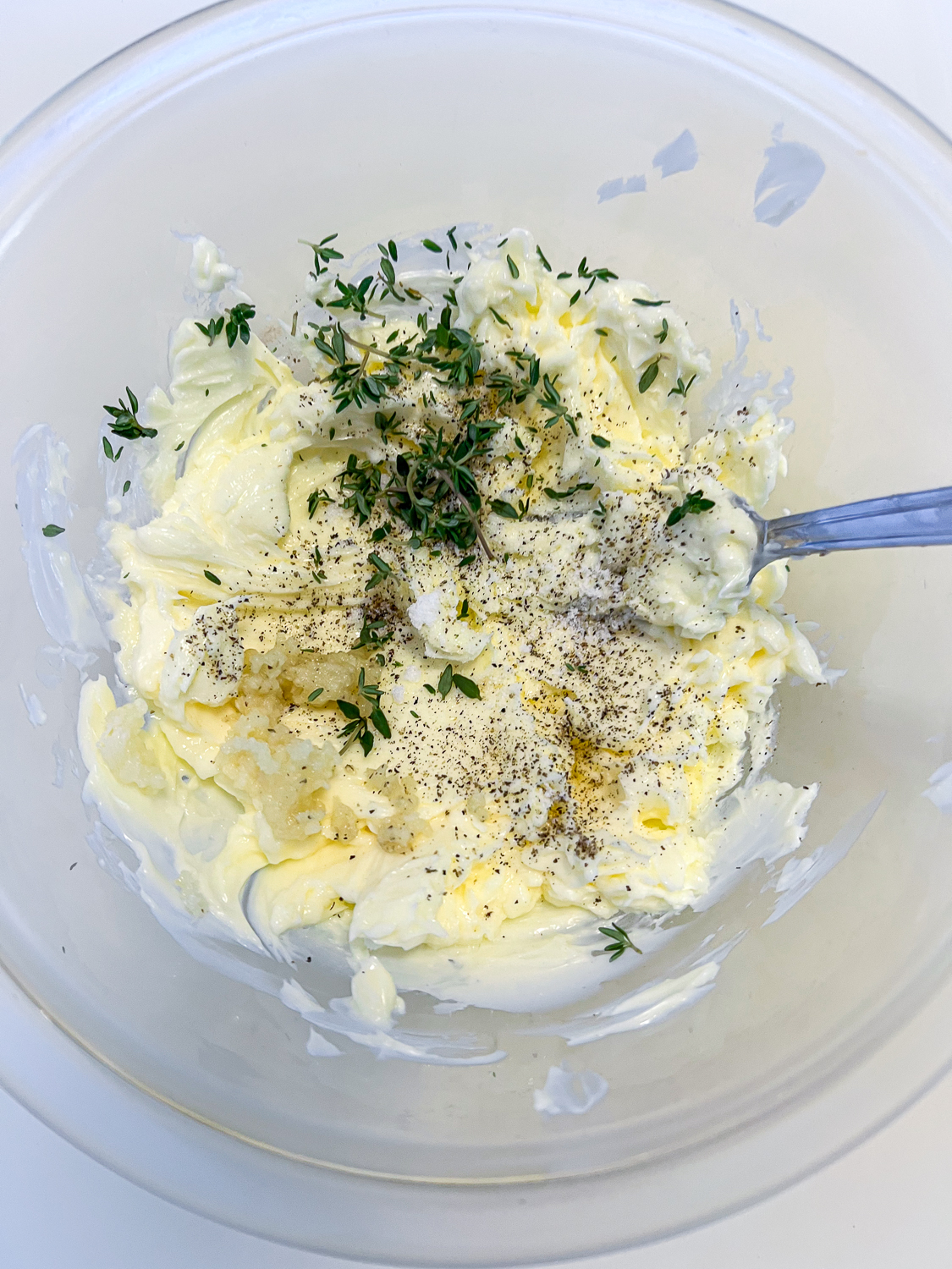 Herb butter being made: softened butter seasoned with salt, pepper, garlic, and fresh herbs ready to be mixed together.