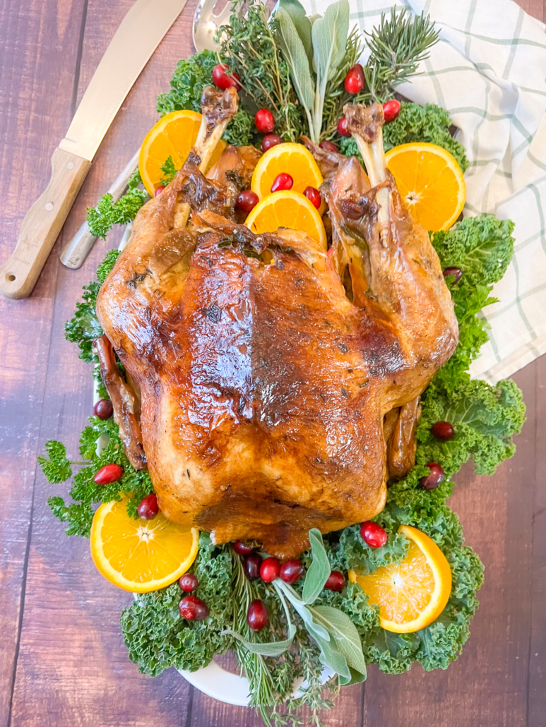 The turkey on a platter with cranberries, oranges, and fresh herbs as garnish.