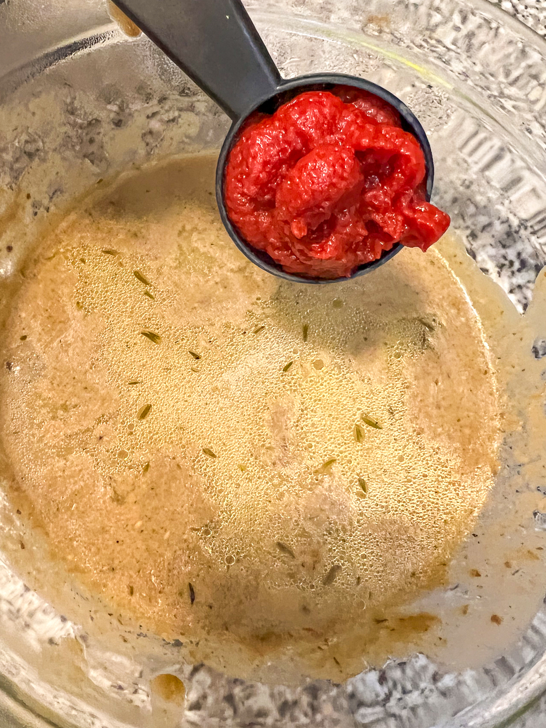 Tomato Paste being added to the liquid for flavor depth.