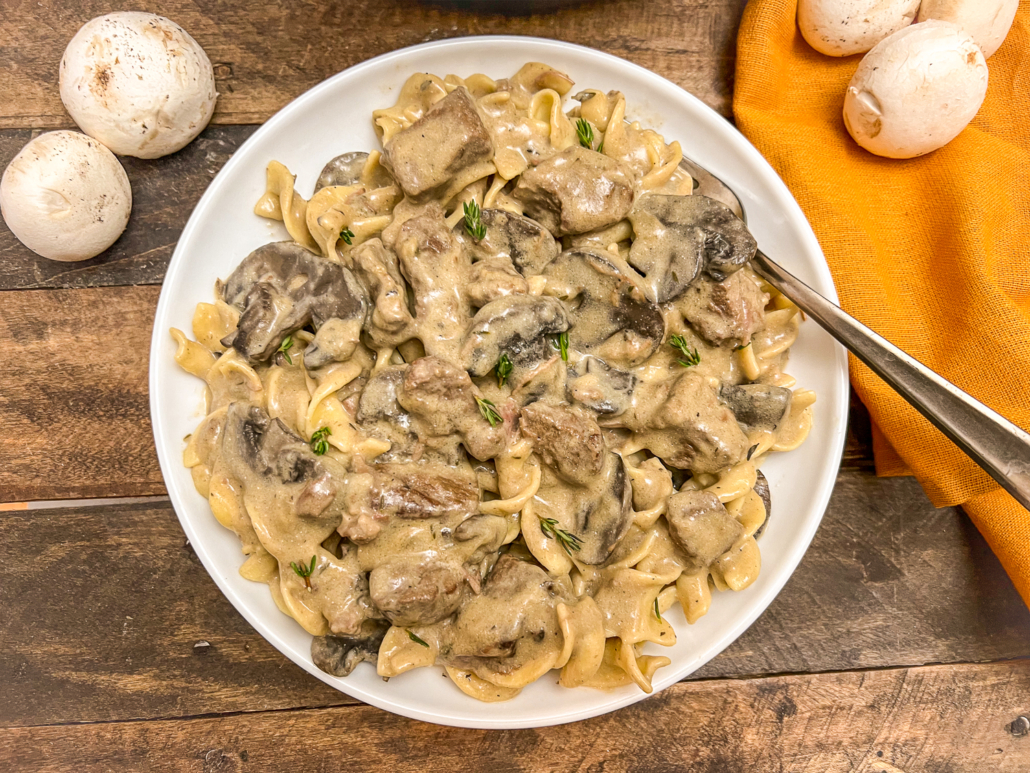 Mushrooms dot the table where a white bowl of beef stroganoff is served.