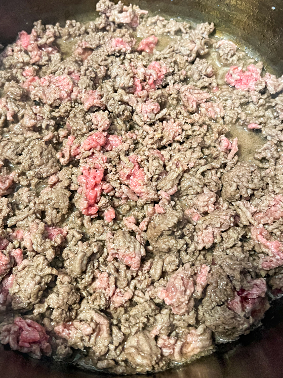 Ground beef browning in a Dutch oven partially cooked.