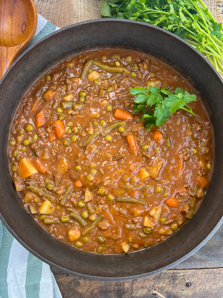 Dutch oven ground beef stew garnished with fresh parsley is ready to be served.