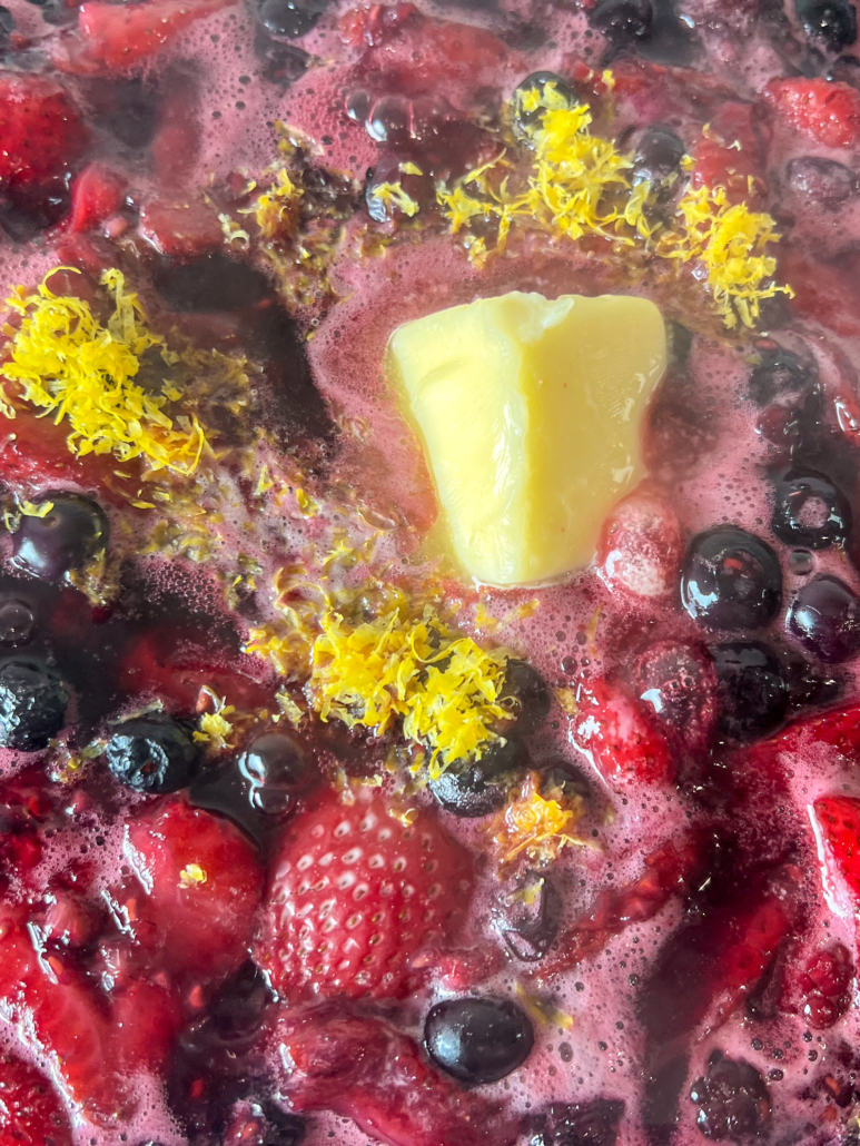Freshly grated lemon zest and butter being mixed into the simmering skillet of fresh berries.