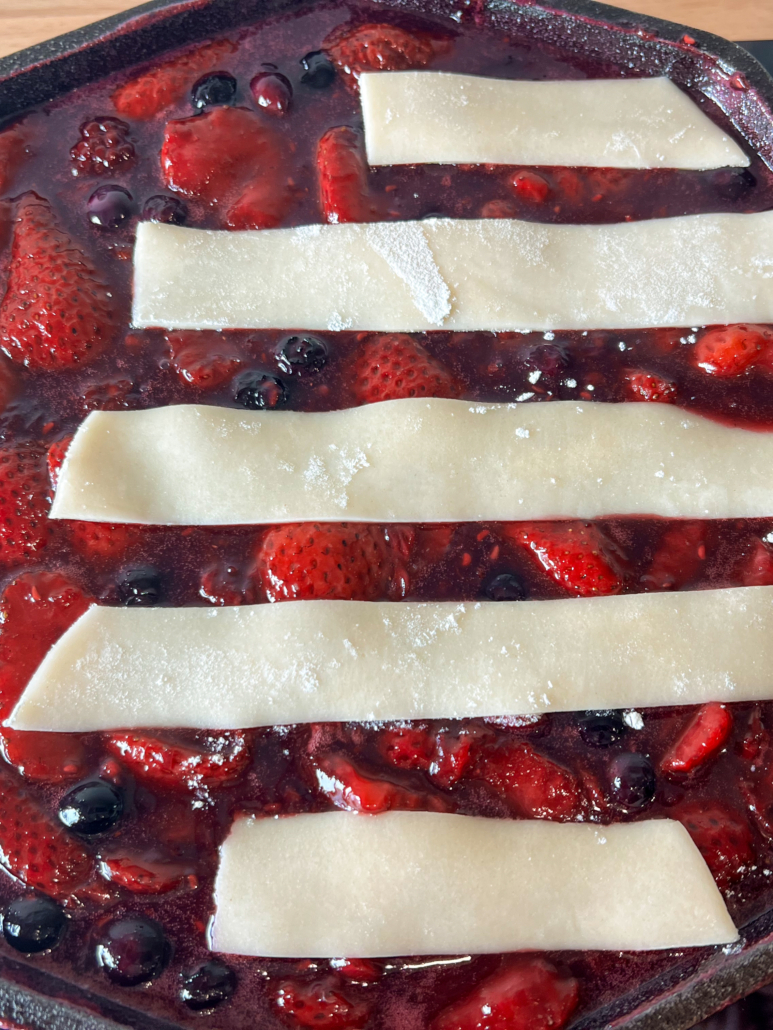 Pie crust has been cut into strips to become the stripes on the flag cobbler and placed on top of the thickened berry compote.