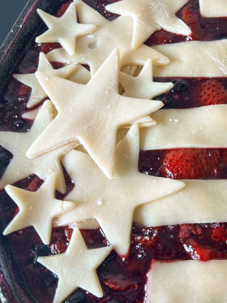 Star-shaped pie crust pieces placed on the left side of the cobbler overlapping each other and the stripes.