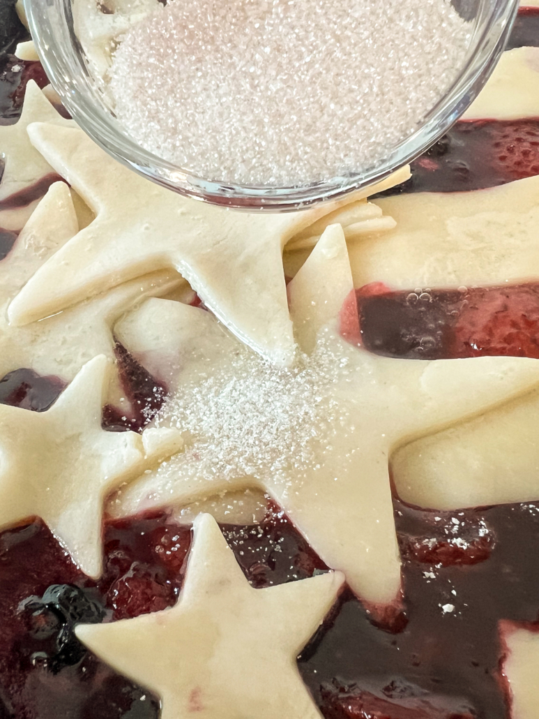 Sparkling sugar being sprinkled over the egg brushed pie crust pieces.