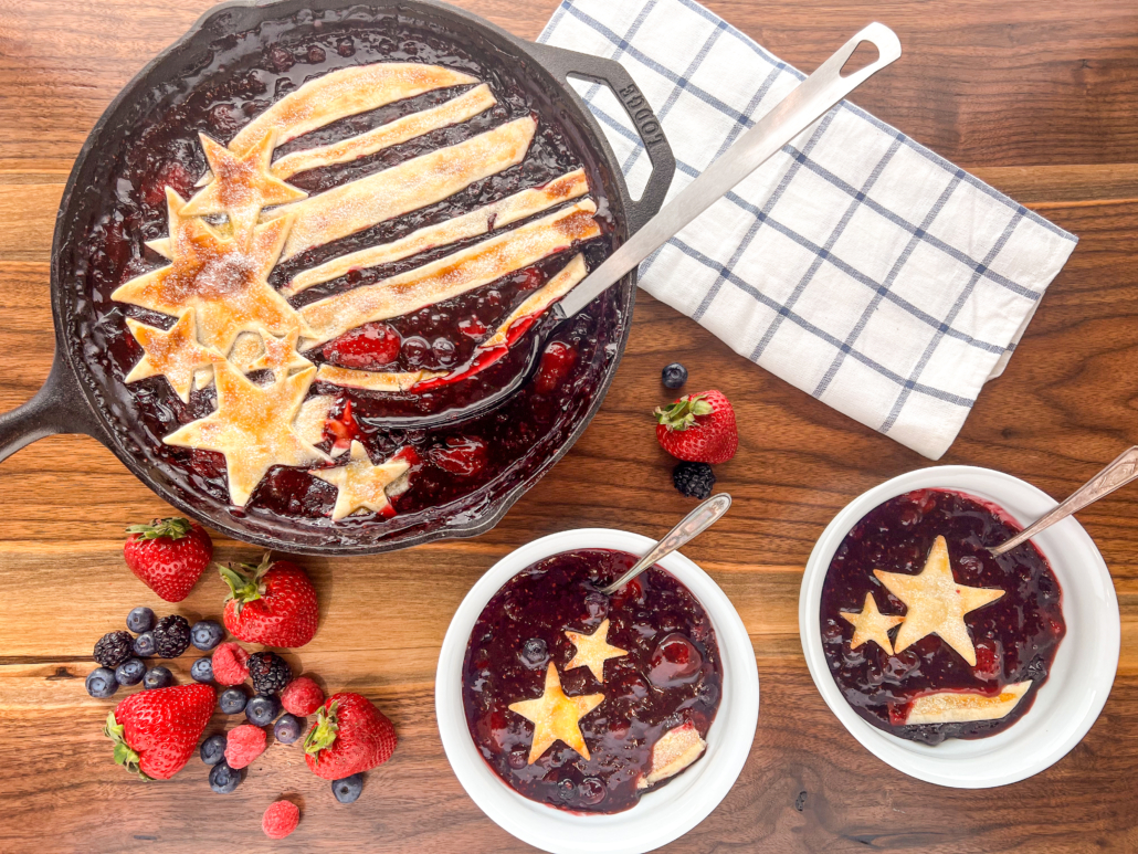 Mixed berry cobbler in a cast iron skillet dished into two white bowls.