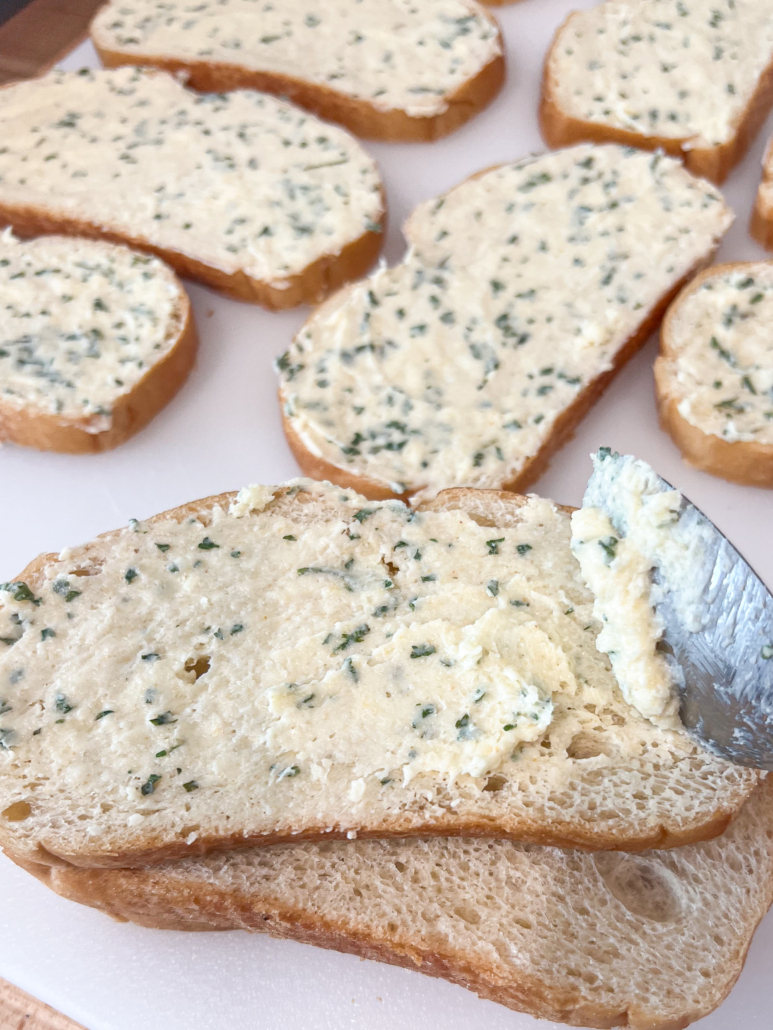 Garlic butter mixture being spread on the bread with the back of a spoon.