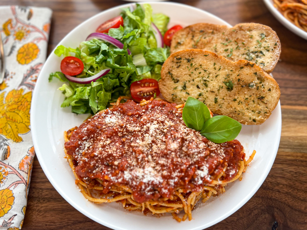 Two slices of garlic bread on a white plate served with a green salad and spaghetti.