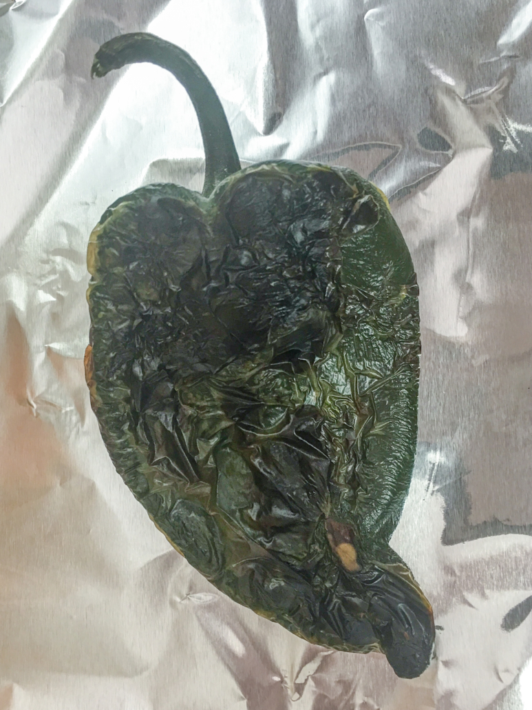 A poblano pepper fresh from roasting is being wrapped in foil to sweat.