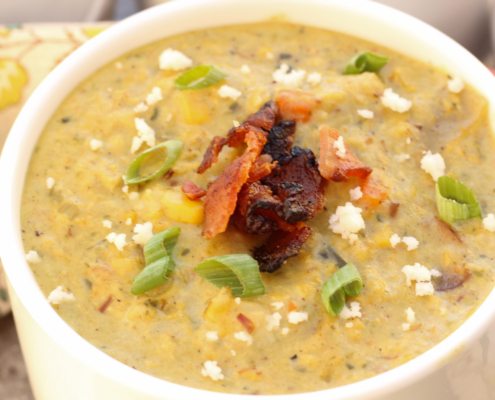 Roasted Poblano Corn Chowder in a white bowl garnished with queso fresco, bacon crumbles, and green onions.