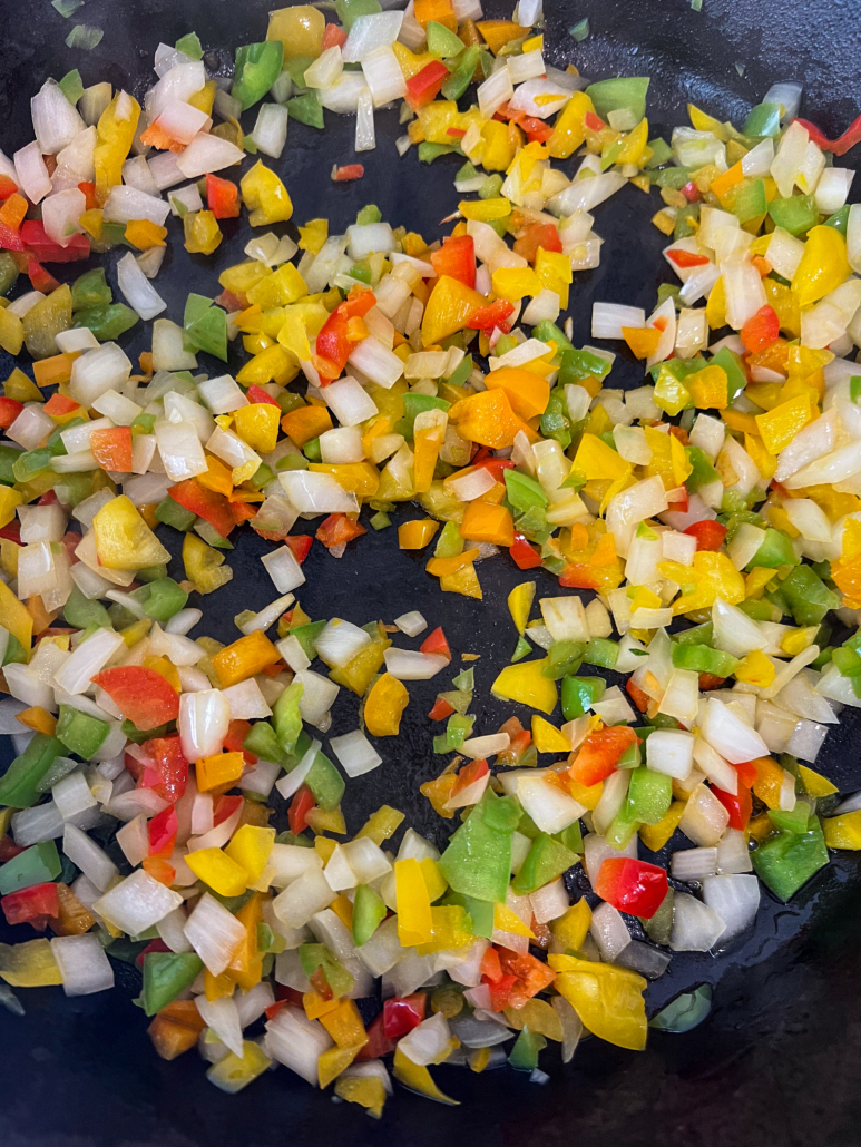 Diced bell pepper tops and diced onions sauteing in a cast iron skillet.