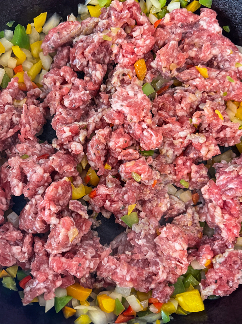 Italian sausage has been crumbled into the skillet to be cooked with the sauteing onions and peppers.