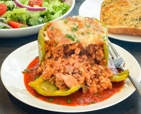 A plated stuffed bell pepper has been sliced open to reveal its meat and rice mixture filling with a salad and garlic bread in the background.