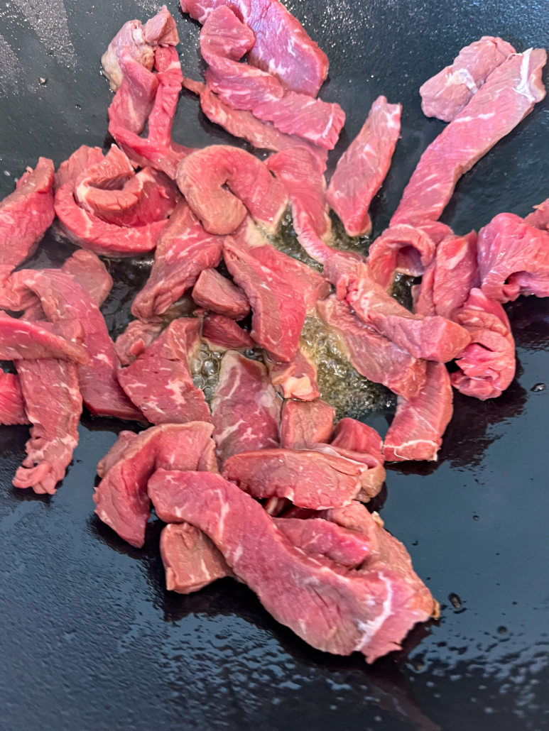 Thinly sliced steak stir frying in a cast iron wok.