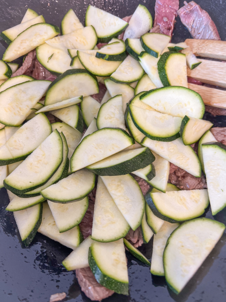 Halved zucchini slices have been added to the the cooking beef.
