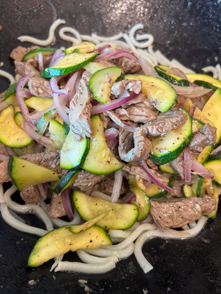 Noodles and the meat mixture are together in the wok.