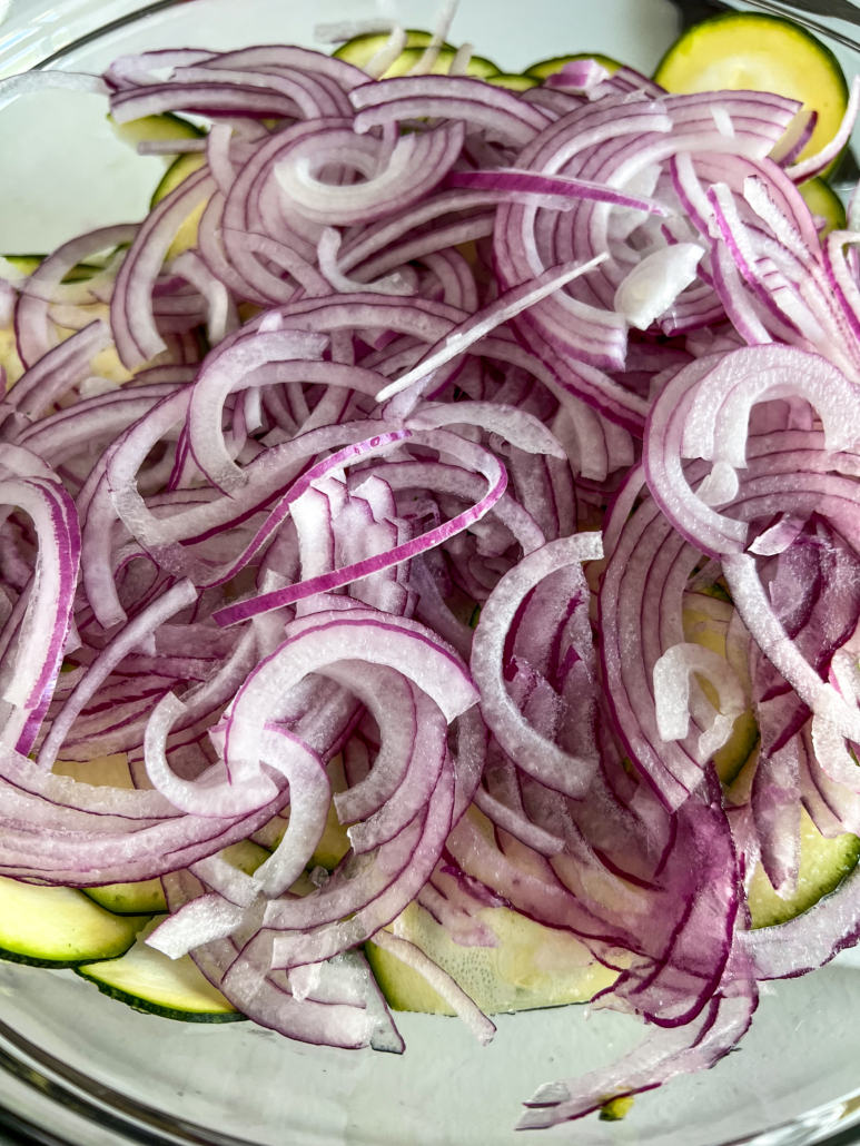 Mandolin sliced zucchini and red onion in a glass bowl.