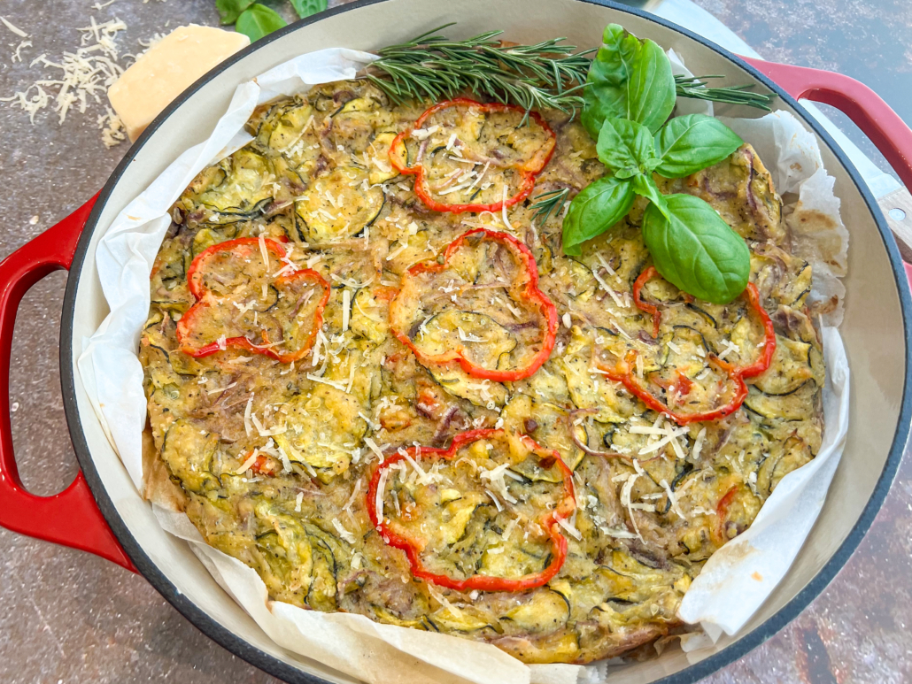 Freshly baked scarpaccia in cast iron garnished with more freshly grated parmesan cheese, basil, and rosemary.