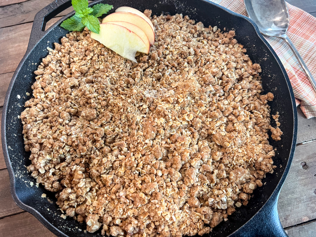 Freshly baked apple crisp in a cast iron skillet garnished with fresh apple slices and mint.